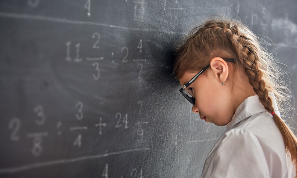 This is a photo of a student with their head on a chalkboard with math written on it.