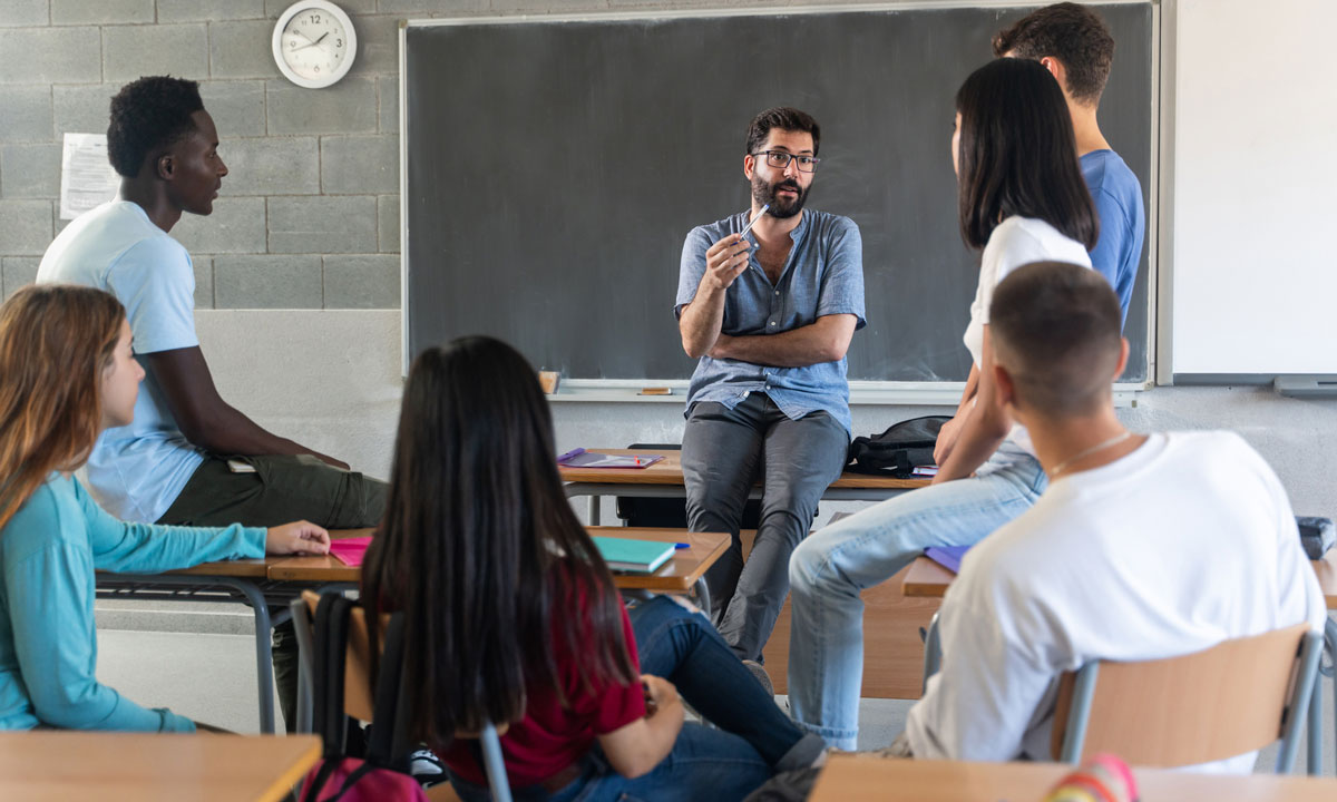 This is a photo of a teacher talking to a small group of students in a circle.