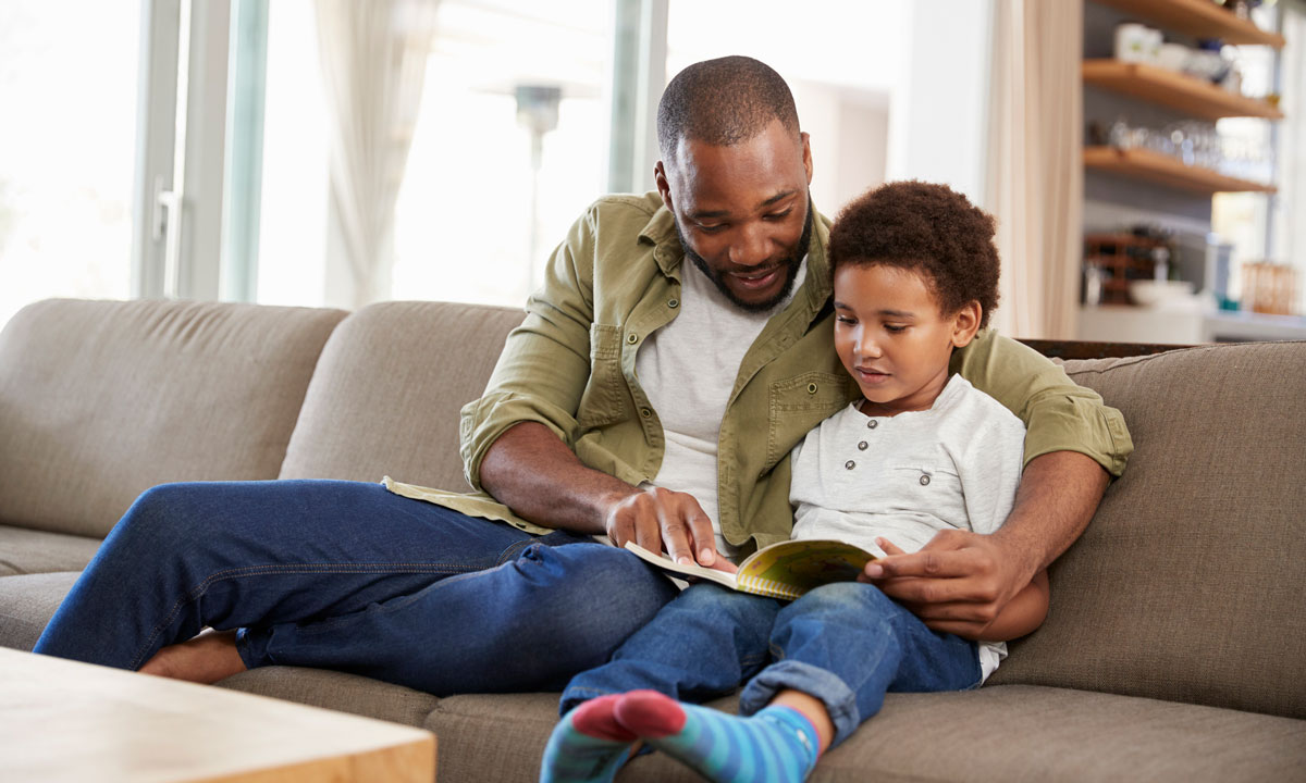 This is a photo of a father and son reading together on a couch.