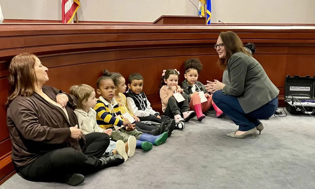 This is a photo of Rep. Kate Farrar sitting on the floor with some children before a press conference.