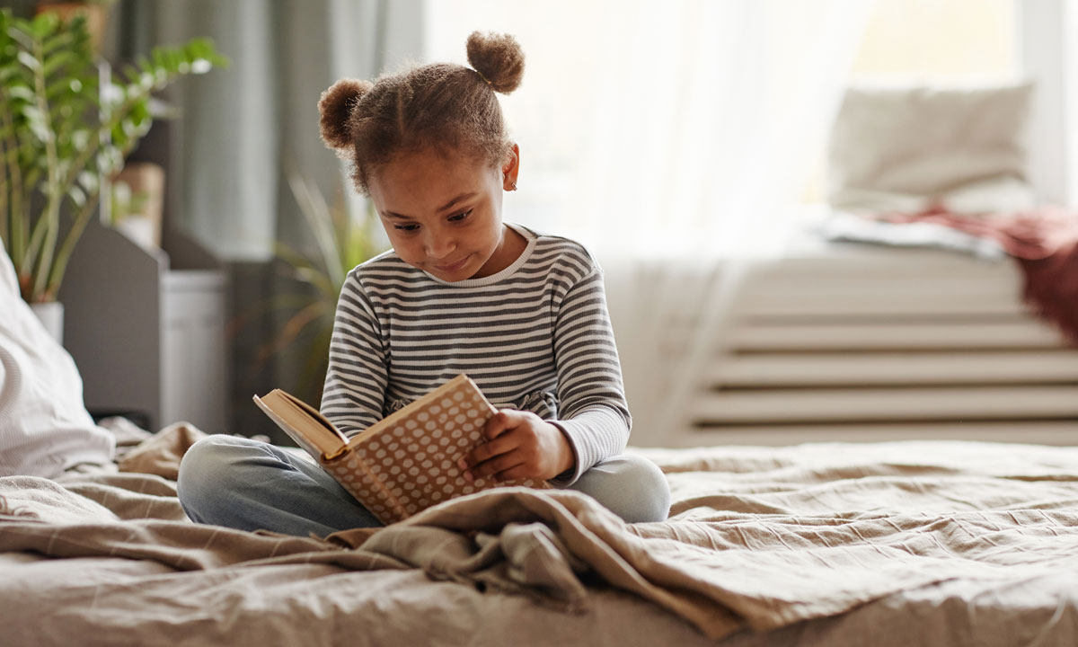 This is a photo of a little girl reading in a bed.