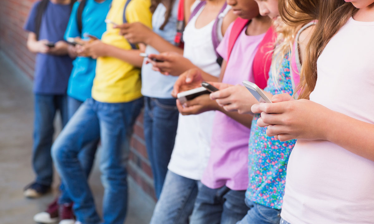 This is a photo of kids in a line all on cellphones.